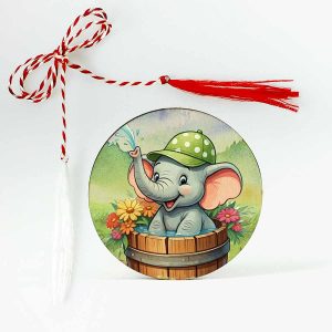 Imagine cu un mărțișor din lemn, reprezentând un elefant vesel care se relaxează într-un butoi cu apă, purtând o șapcă verde și fiind înconjurat de flori colorate.