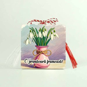 Imagine cu un martisor din lemn tip brosa personalizat cu o vaza roz prafuit legata cu snur de martisor in care sunt cativa ghiocei dleicati. Martisorul are scris me sajul O primavara frumoasa!